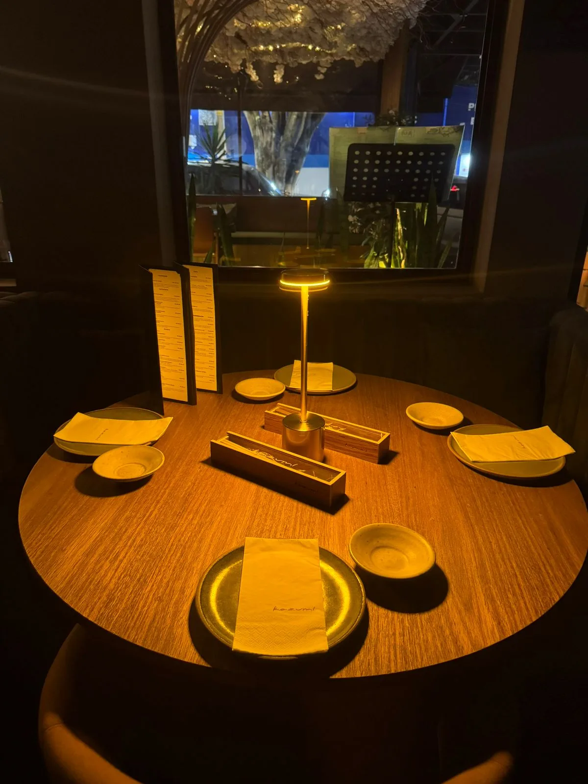 Mesa posta no Kazumi com cardápio e luminária dourada